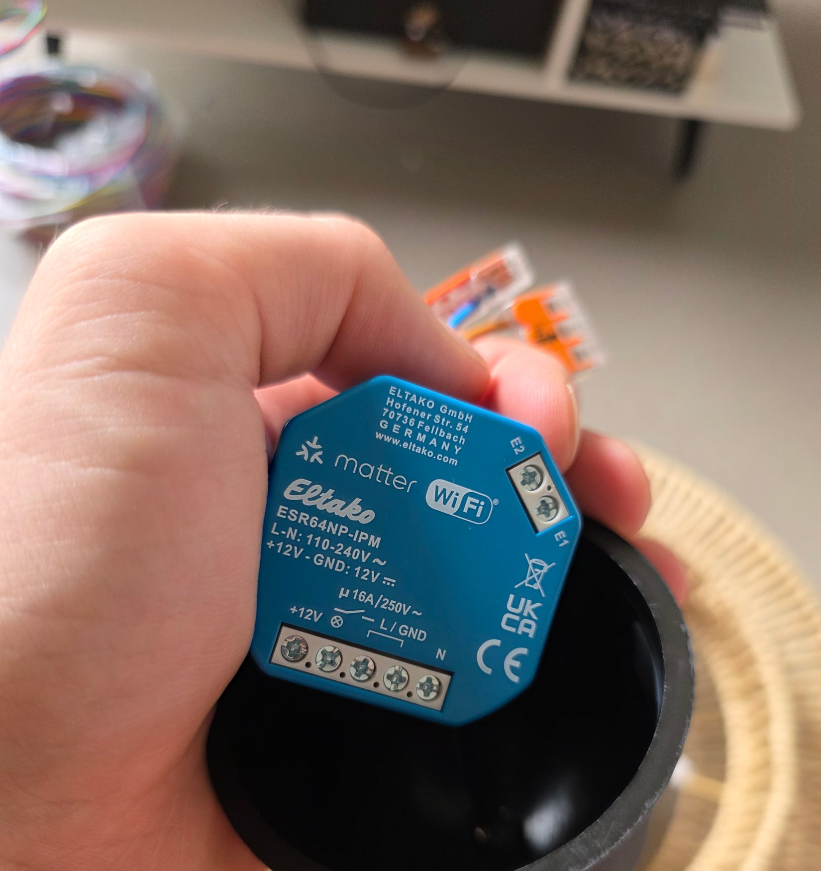 Micromodulo Eltako ESR64NP-IPM tenuto in mano, con i suoi riferimenti E1 ed E2 e la sua fila di morsetti a vite.