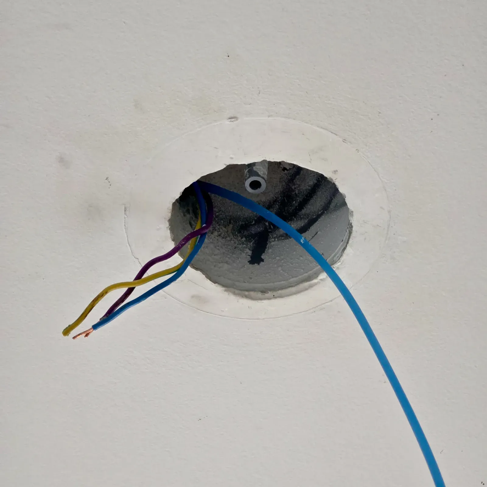 White plastic conduit and blue nylon draw wire visible through a ceiling opening during a separate wiring job