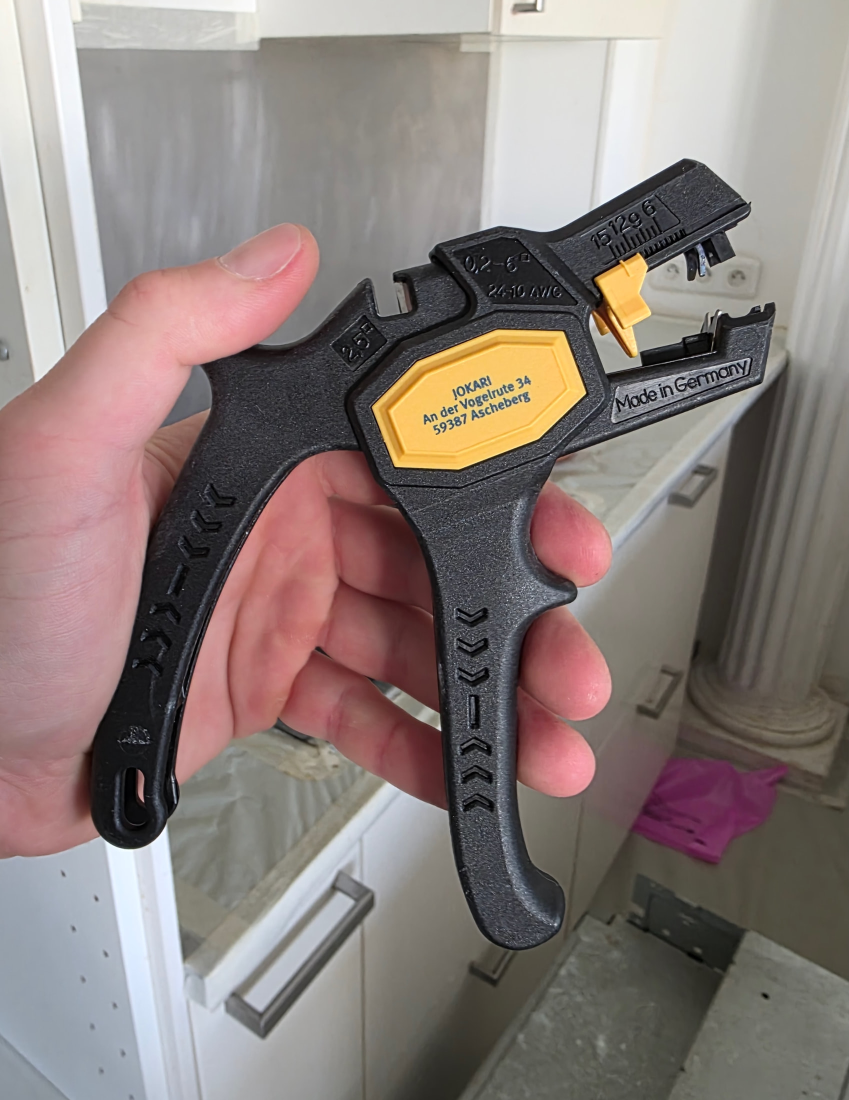 Pinza automatica spelafili Jokari Super 4 Plus nera e gialla tenuta in mano, incisioni tecniche visibili