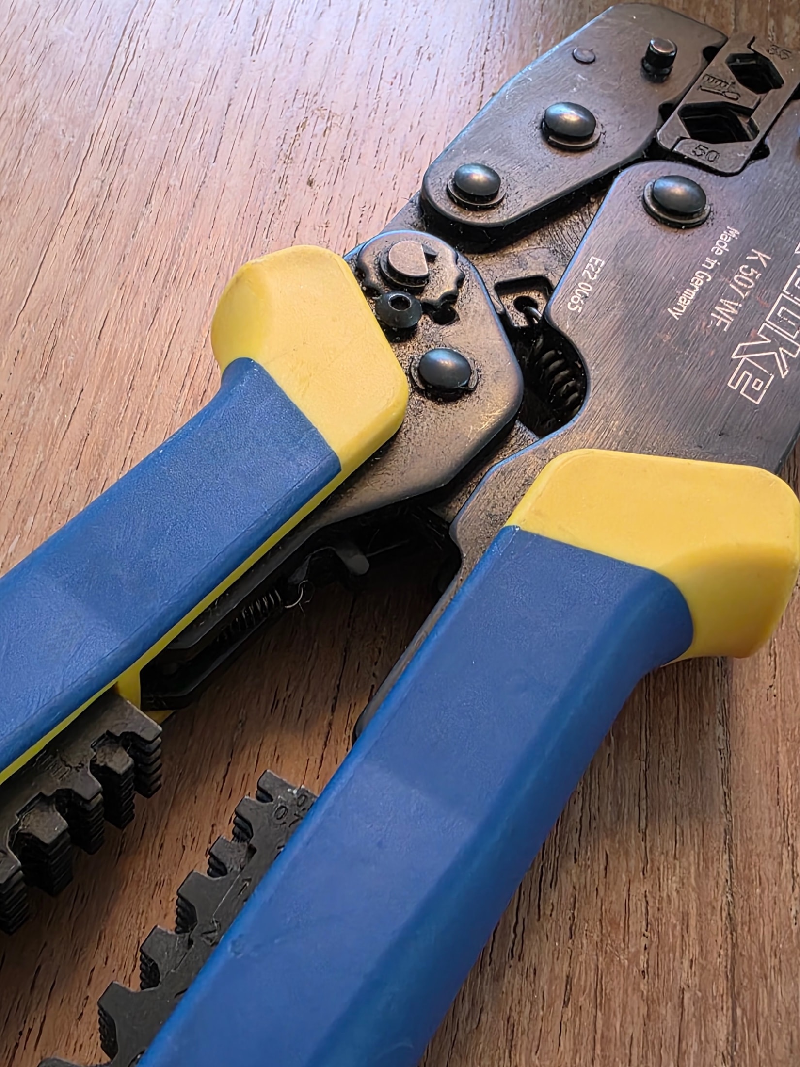 Detalle de la articulación de la pinza de crimpar Klauke K 507 WF, empuñaduras azules y amarillas, grabado del modelo y mordazas dentadas
