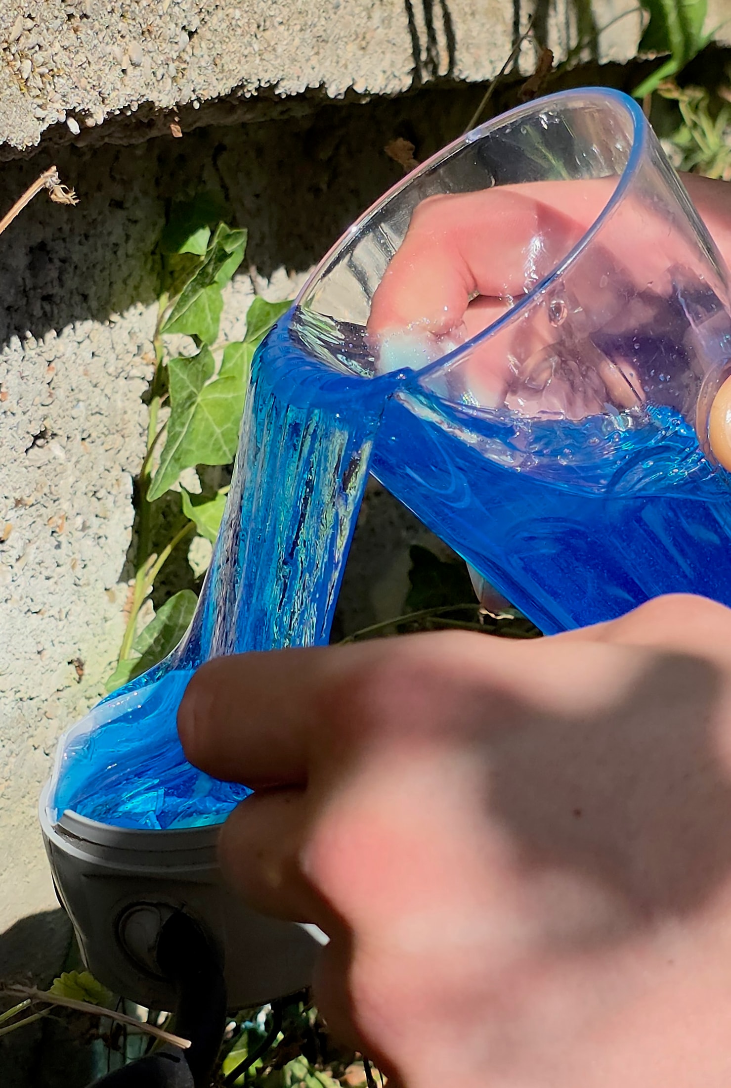 Dito che tocca il Magic Gel blu in una scatola rotonda mentre viene versato da un bicchiere tenuto a mano