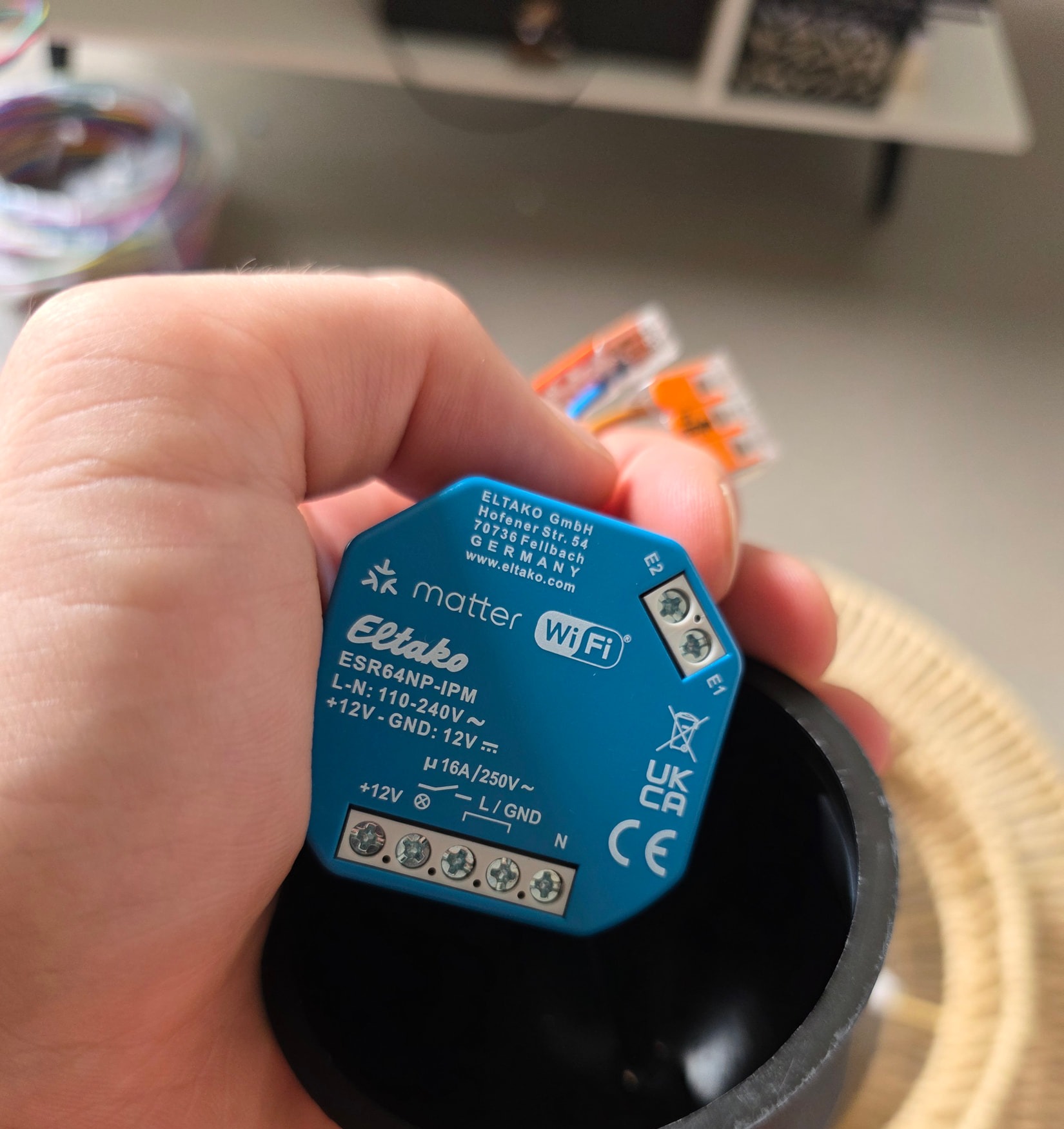 Micromódulo Eltako ESR64NP-IPM sostenido en la mano, mostrando su etiqueta, su bornera y el marcado matter WiFi.