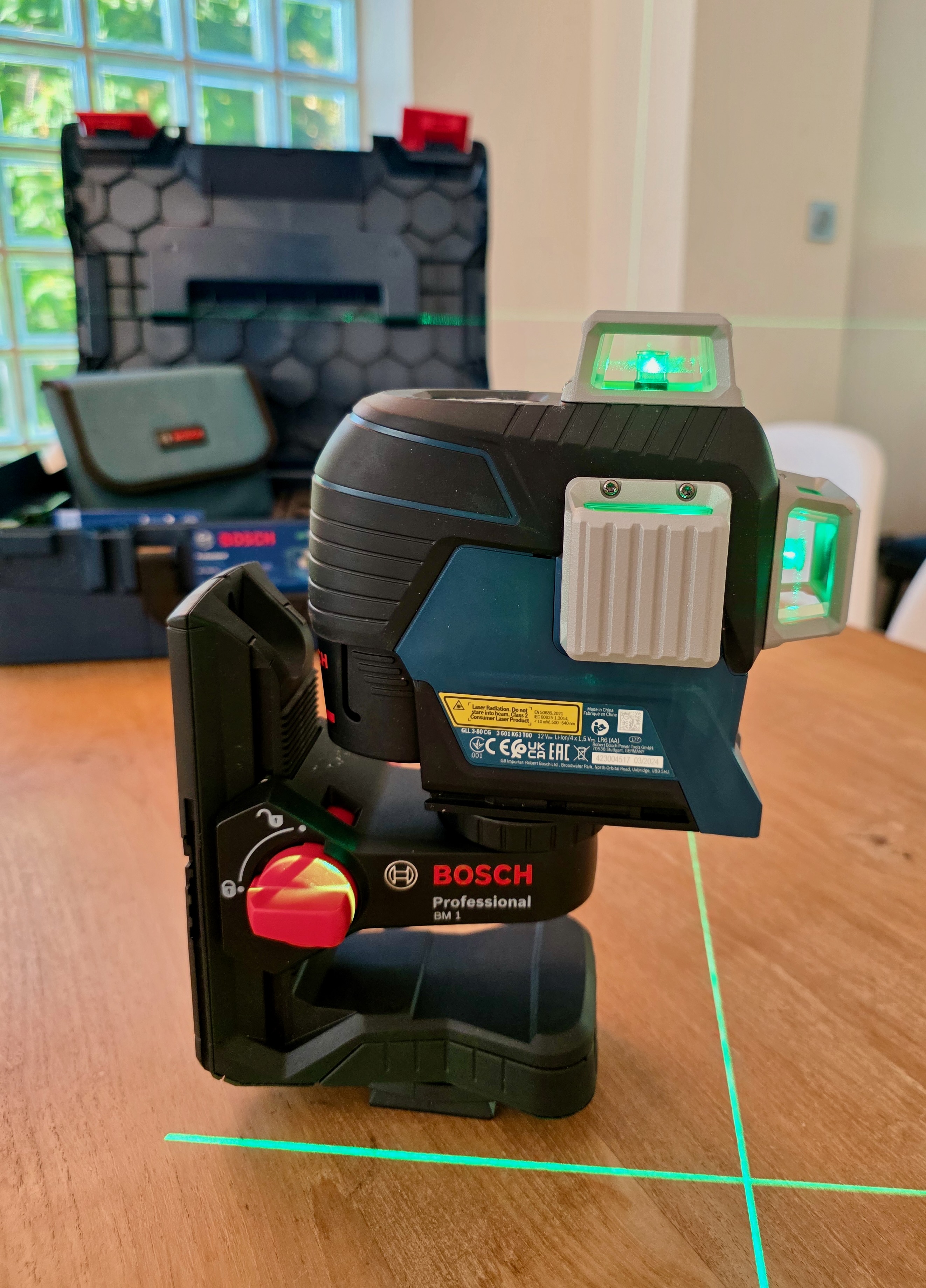 Bosch laser level set on a table, switched on, projecting a green laser line onto the wall