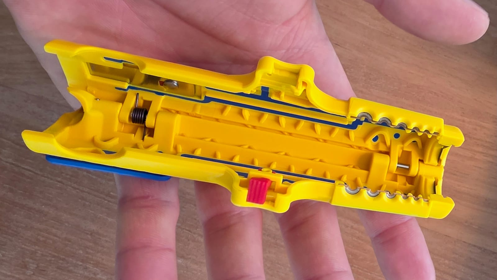 Mano che tiene lo spelafili Jokari giallo aperto, mostrando il meccanismo interno e il pulsante rosso