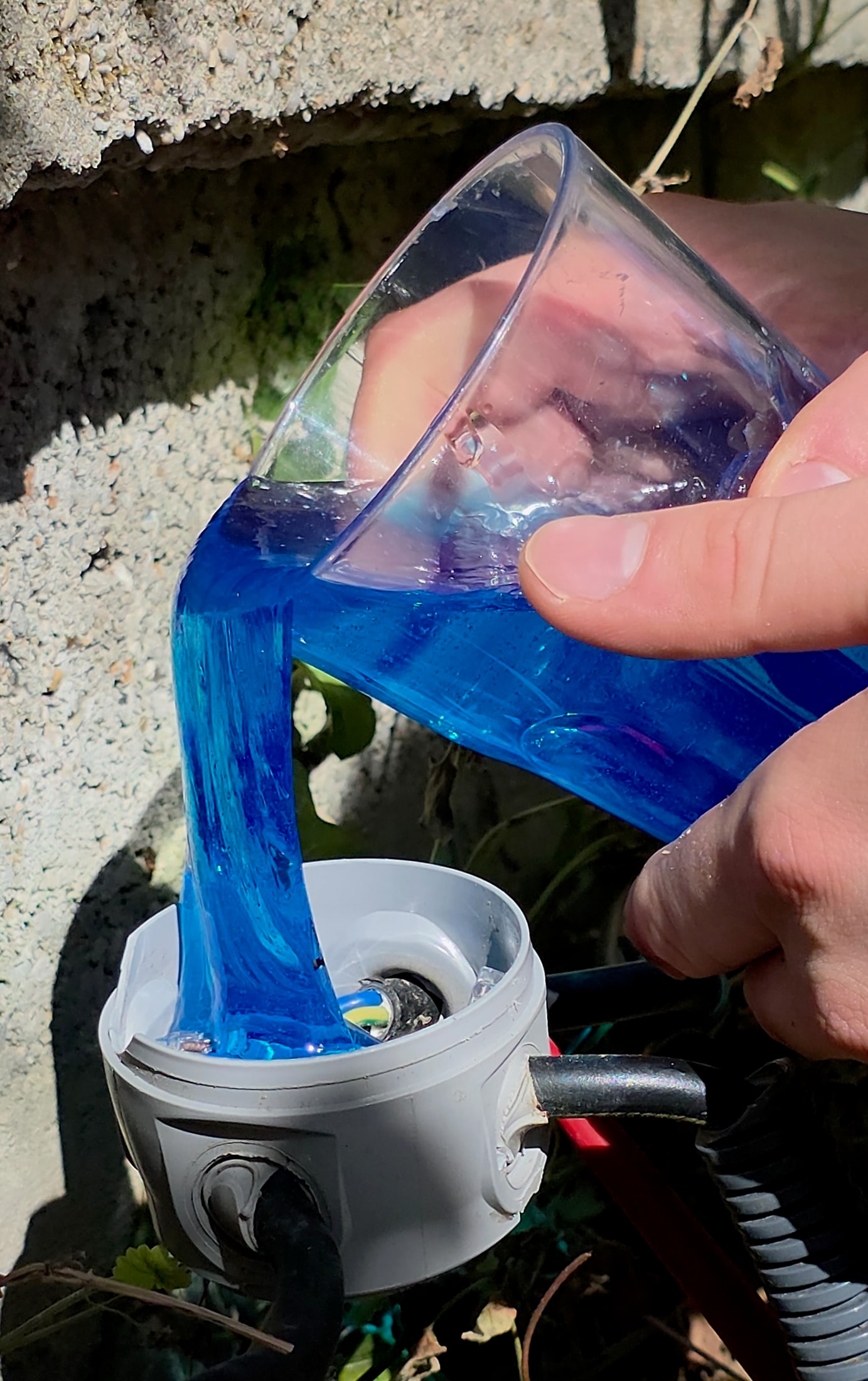 Mani che versano Magic Gel blu in una scatola grigia rotonda all'aperto vicino a un muro in cemento
