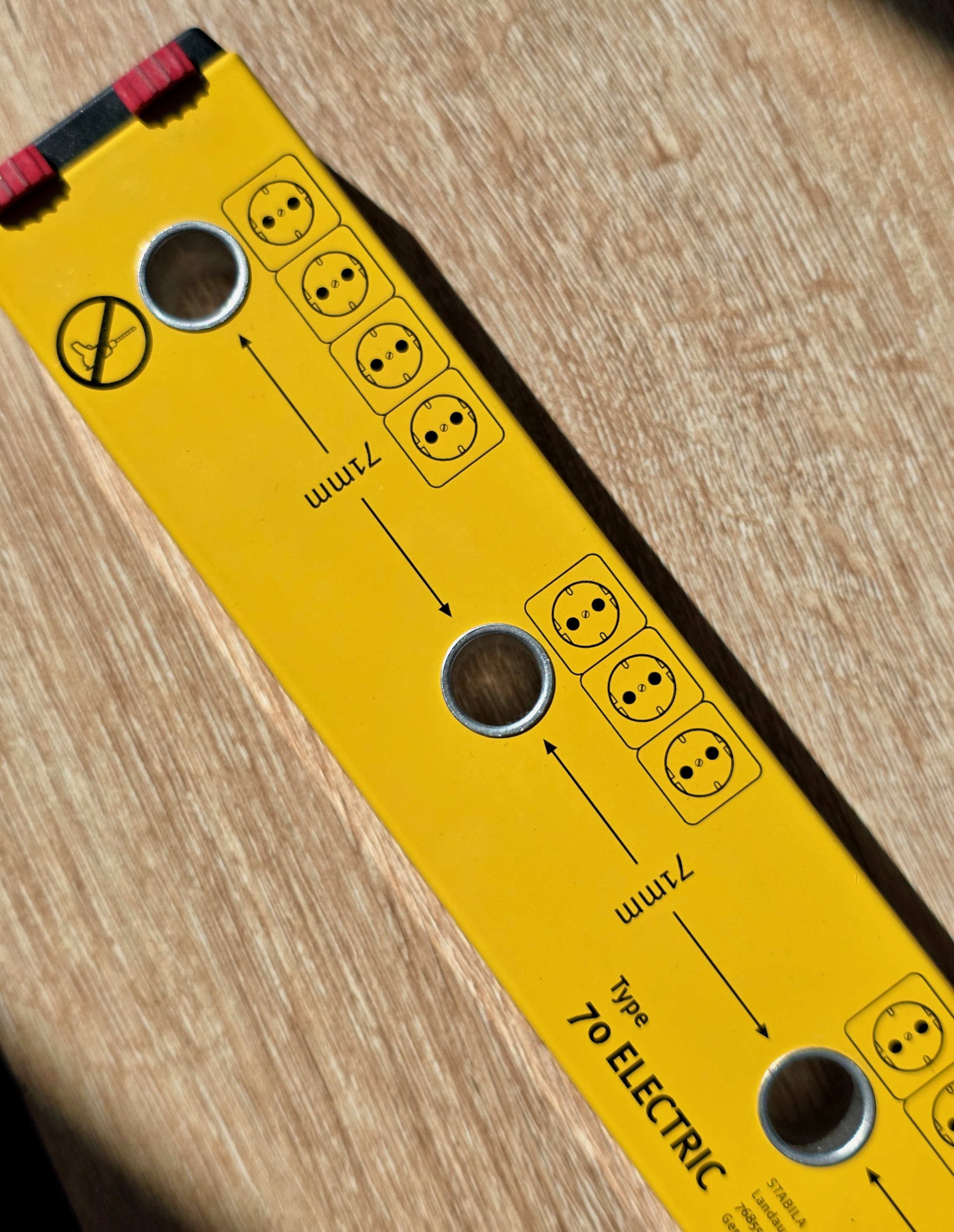 Reverse side of a yellow STABILA Type 70 Electric level showing its circular marking guides and dark contact pads on a wooden surface