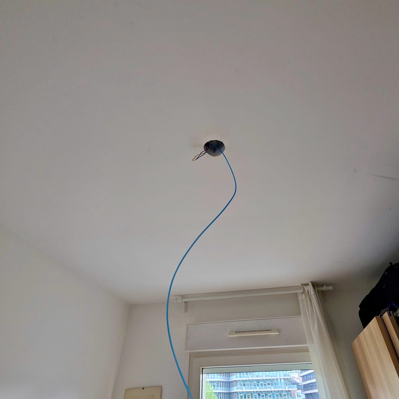 Blue nylon draw tape coming out of a ceiling hole with stripped conductors, during a cable pull