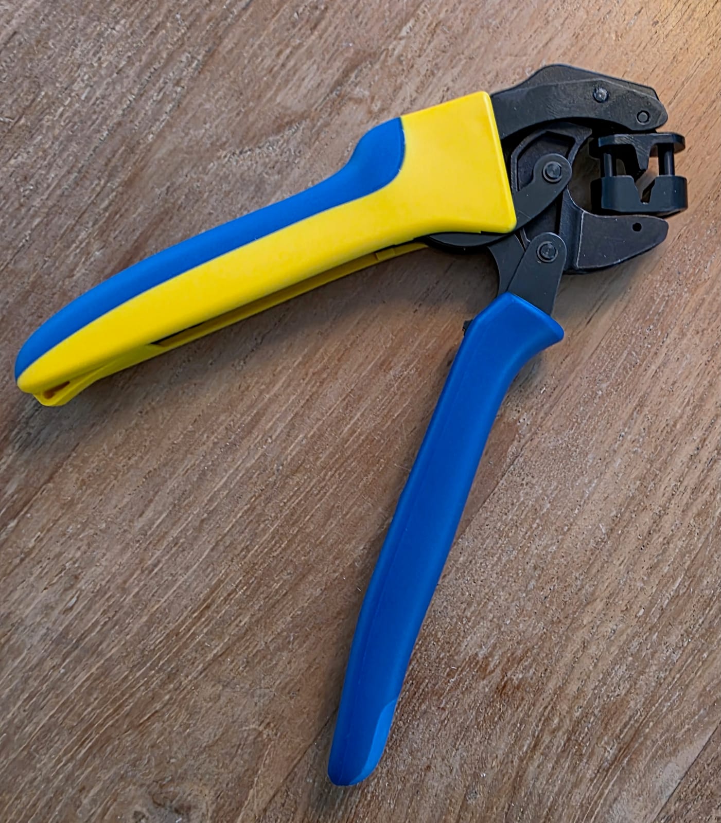 Pinza Klauke K32 abierta sobre una superficie de trabajo de madera, empuñaduras azul y amarilla y cabeza de crimpado negra