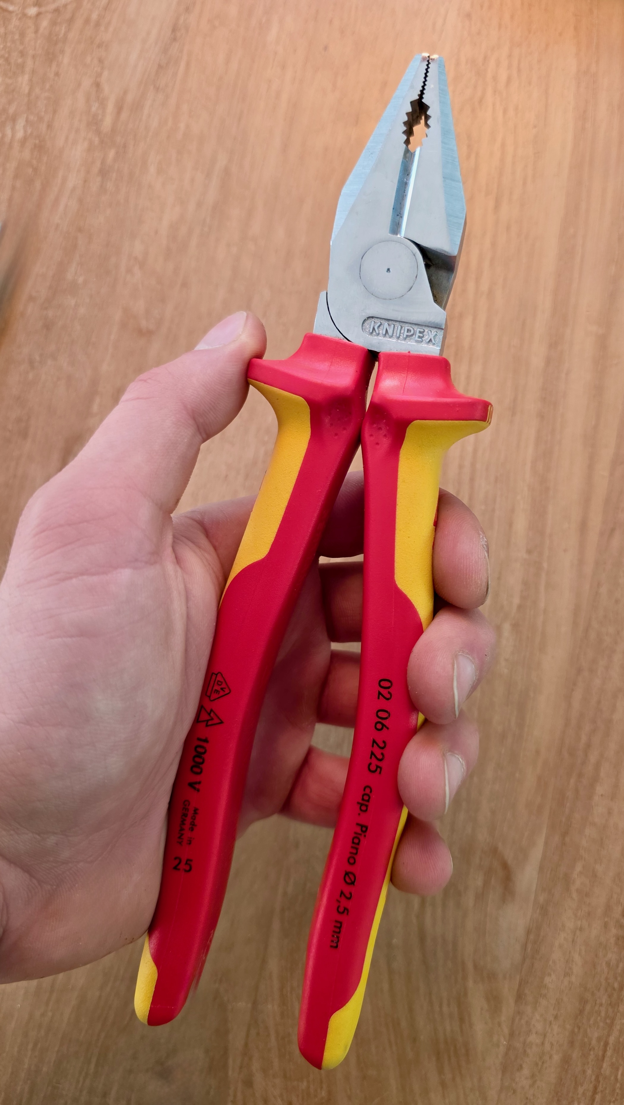 Alicate universal VDE Knipex 02 06 225 sostenido en la mano, símbolo 1000 V impreso en el mango amarillo