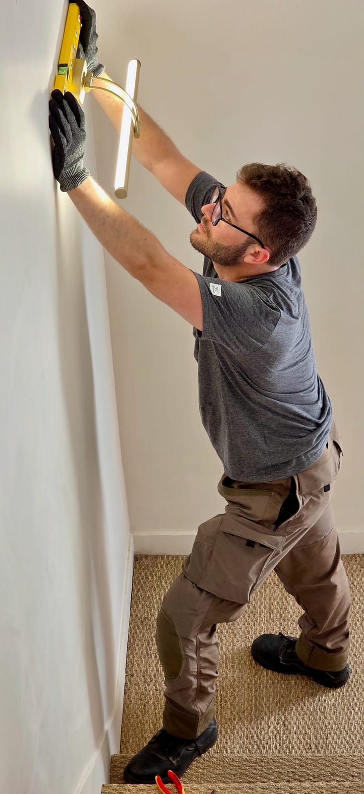 Théo Desrousseaux ajuste un luminaire avec un niveau Stabila en intérieur, pantalon Ilkott