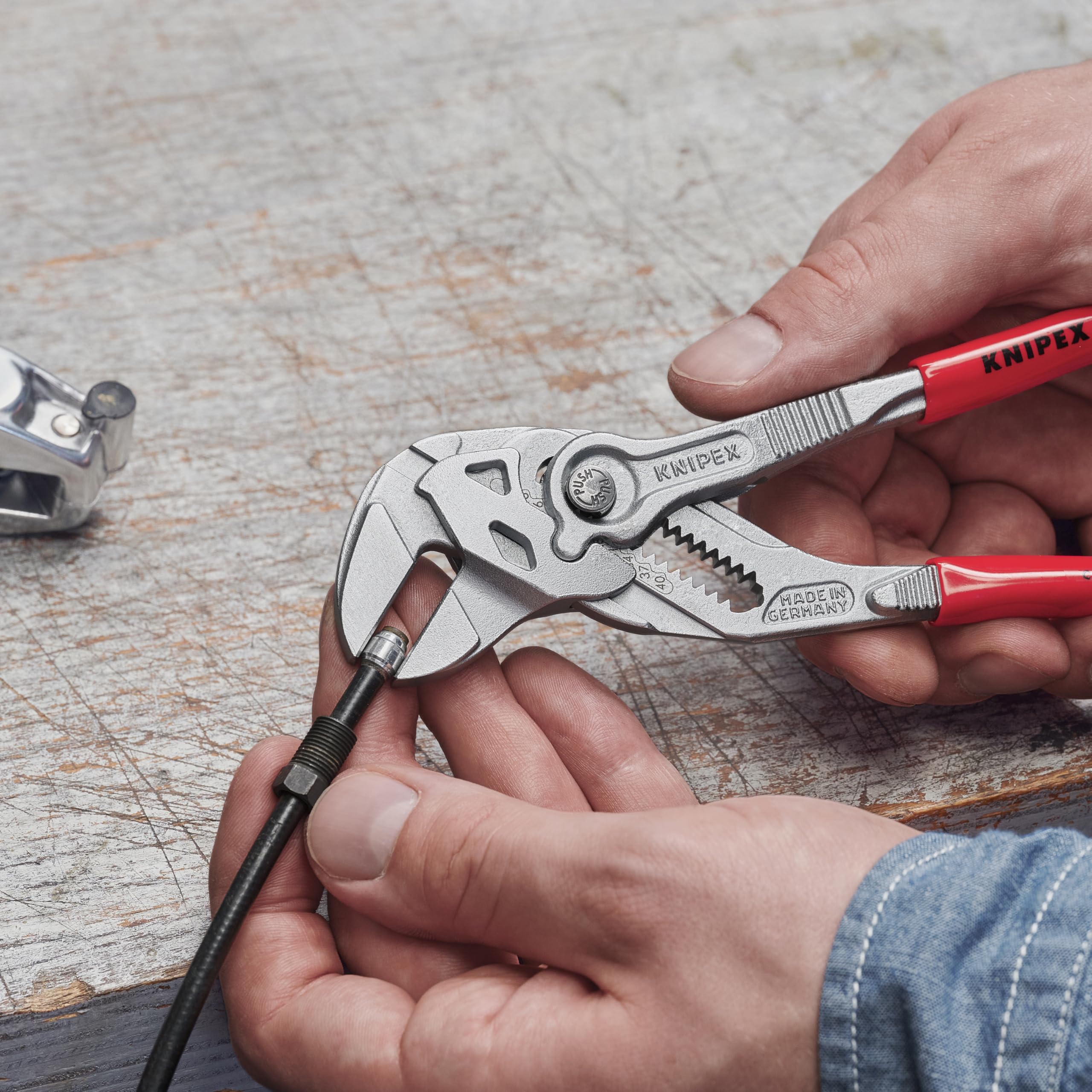 Manos usando una llave-pinza KNIPEX con mangos rojos para apretar una tuerca sobre un cable.
