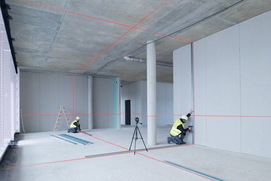 Workers aligning partition framing with a line laser on a tripod