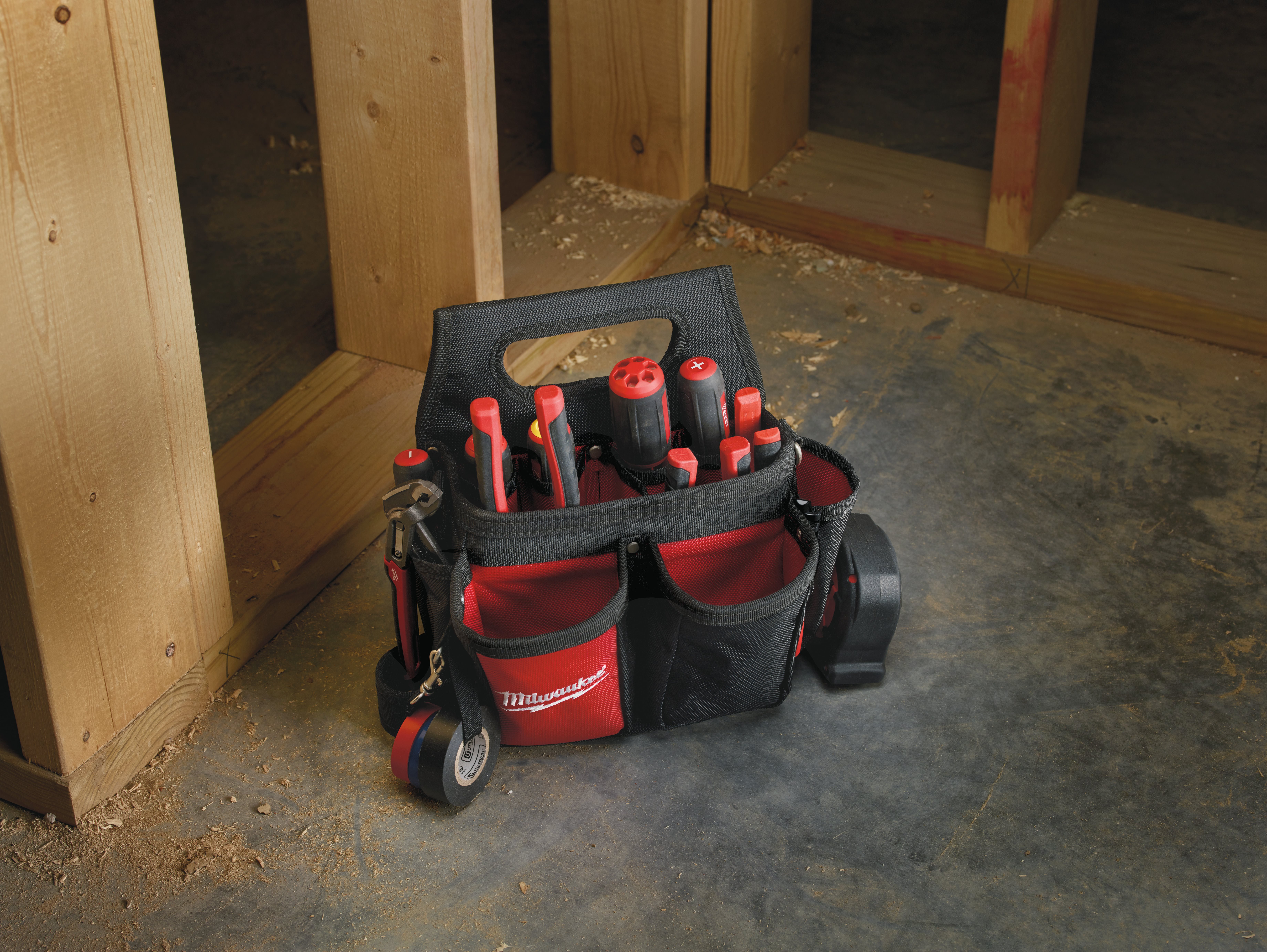 An open black and red Milwaukee tool bag filled with screwdrivers, sitting on the ground at a timber construction site