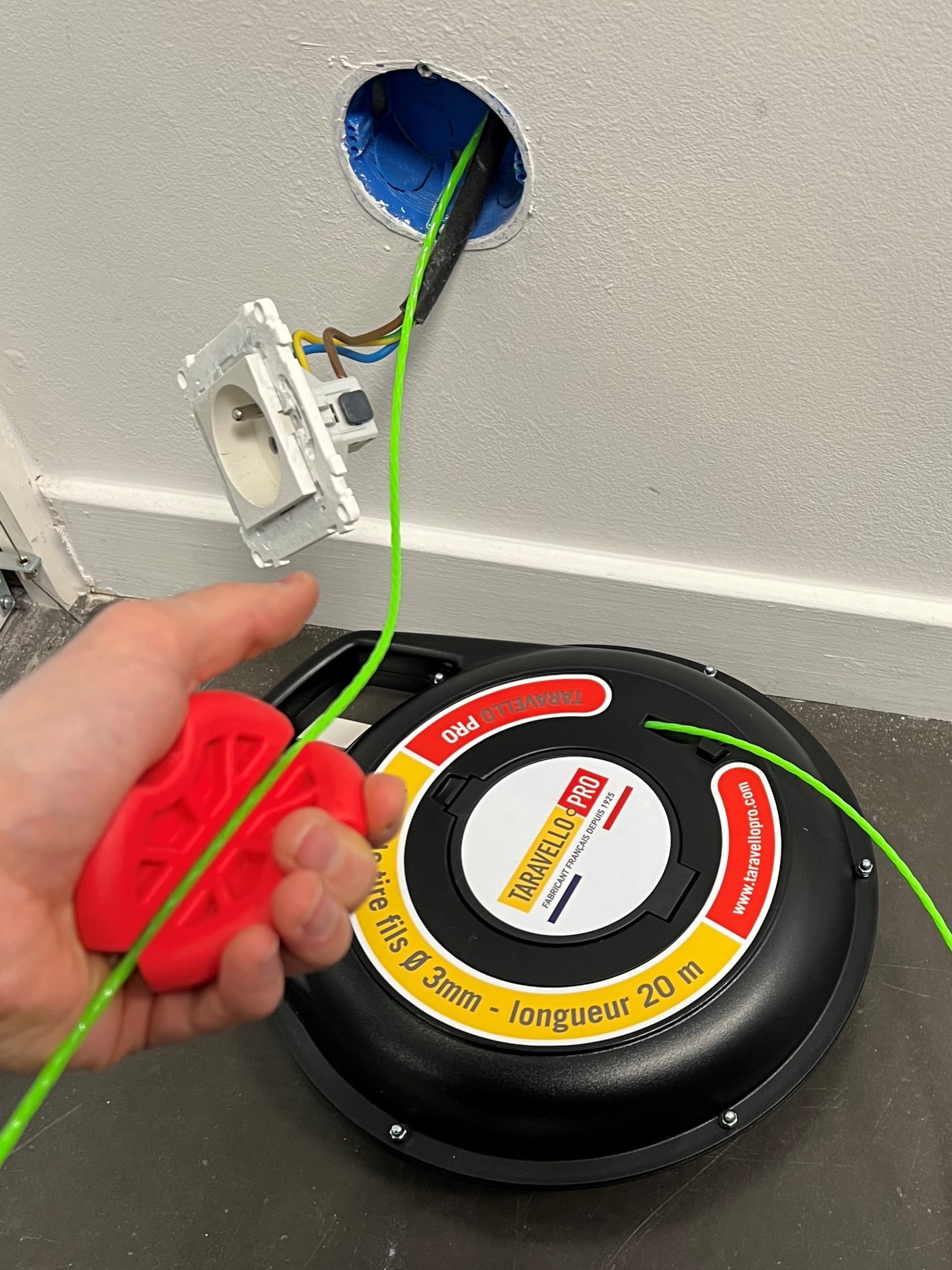 Hand holding the red accessory attached to the green Taravello Pro wire coming out of a flush-mounting box