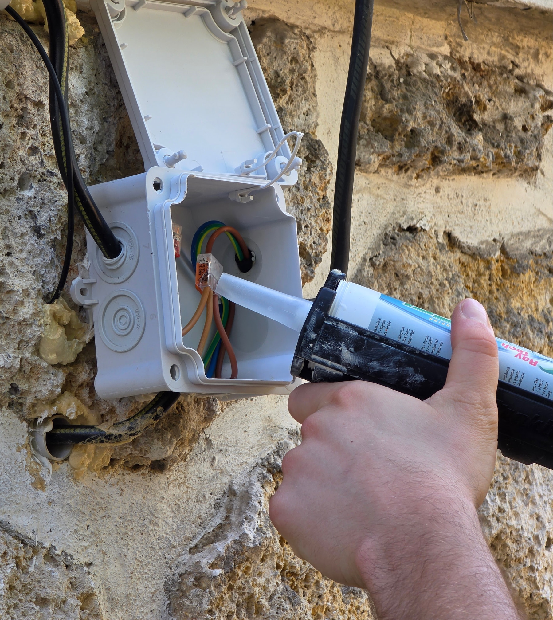 Application de gel d'étanchéité Raytech dans une boîte de dérivation extérieure fixée sur un mur en pierre