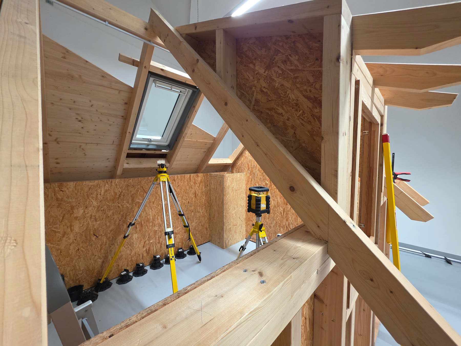 Timber-frame house model with a rotary laser and a STABILA laser level set up on tripods