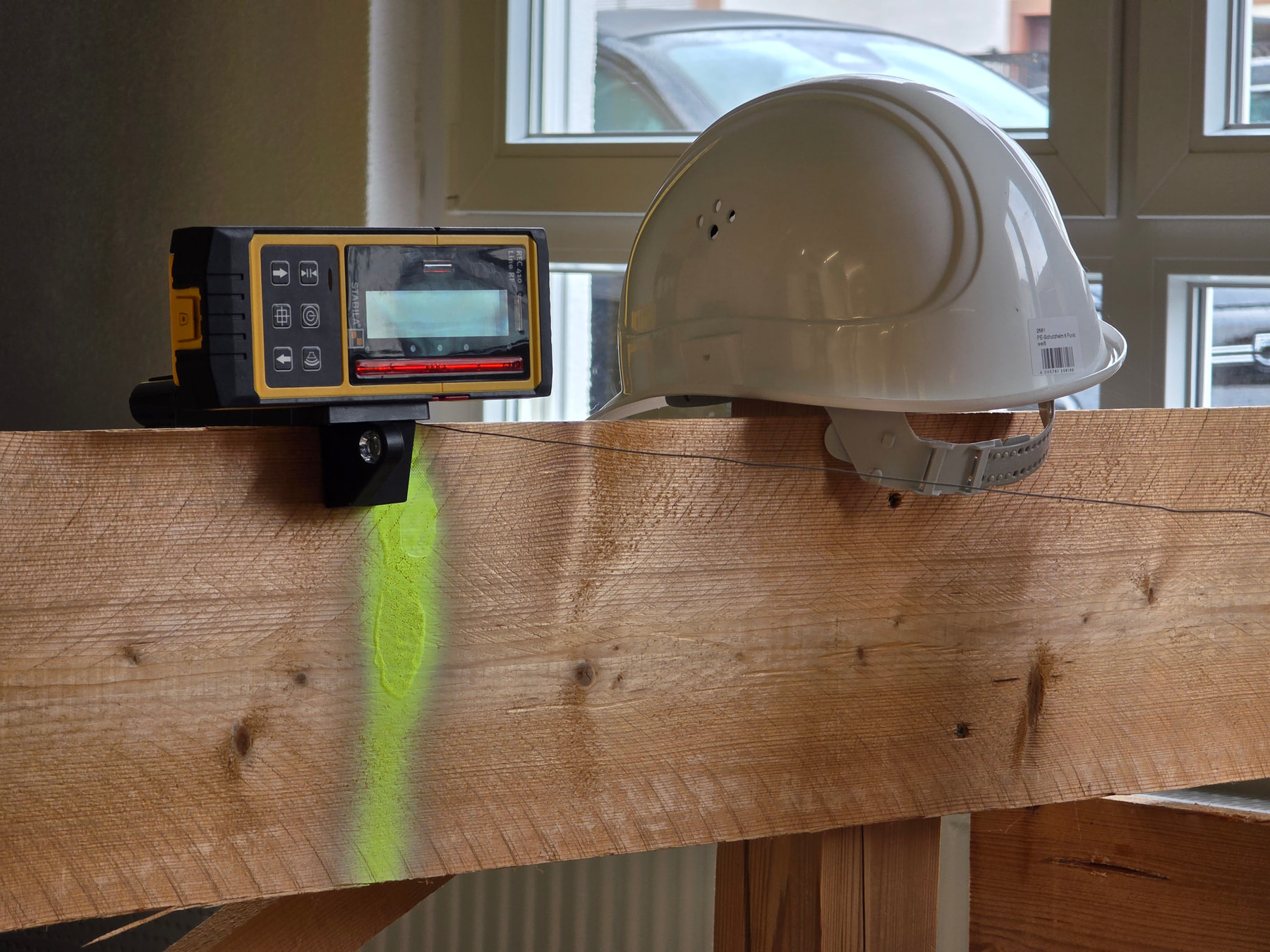 STABILA laser receiver mounted on a wooden beam with a green laser line projected and a white hard hat